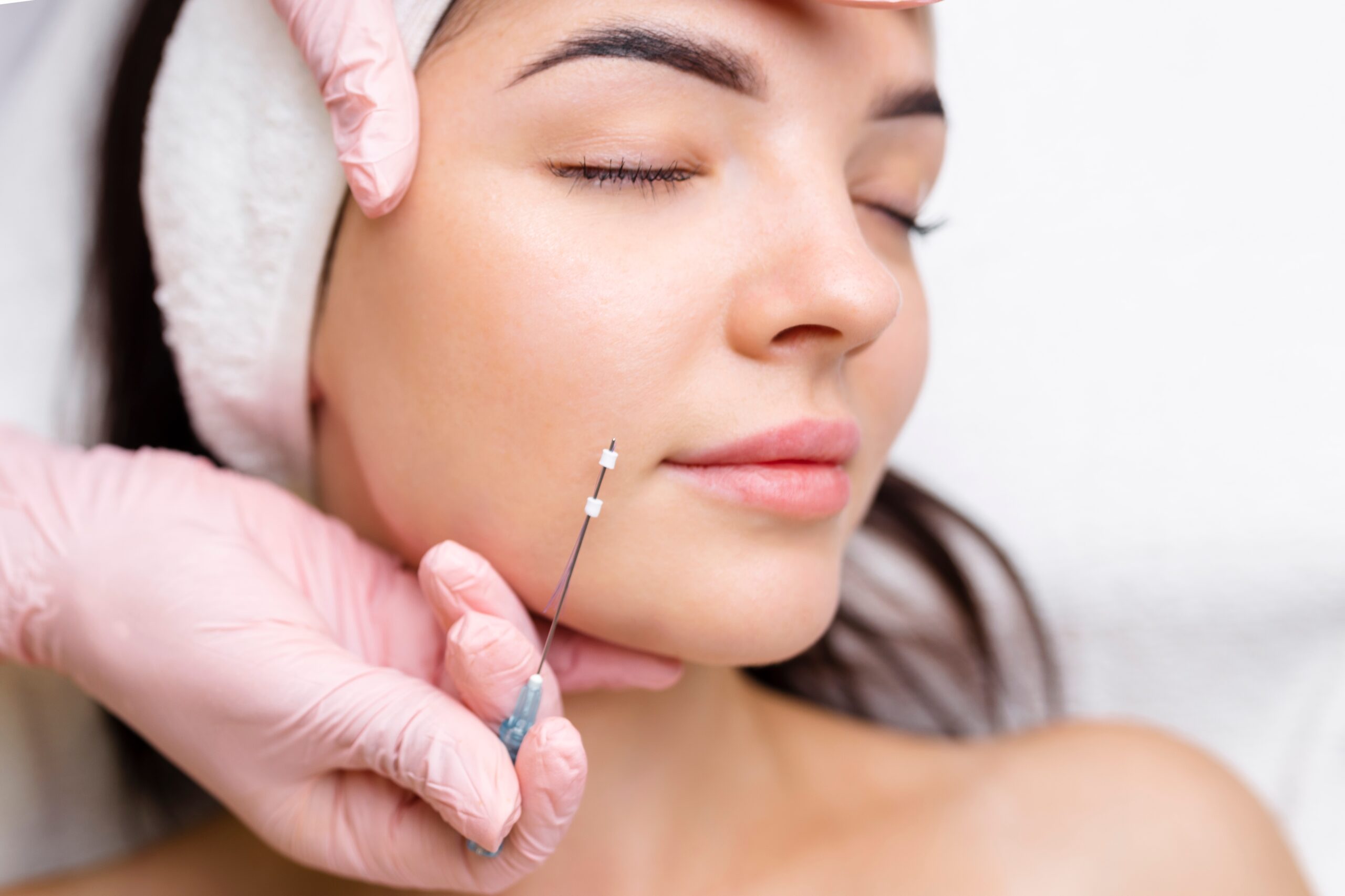 Aesthetic treatment session showing a woman receiving a cosmetic injection on her cheek, performed by a professional wearing pink gloves, highlighting skincare and beauty procedures.